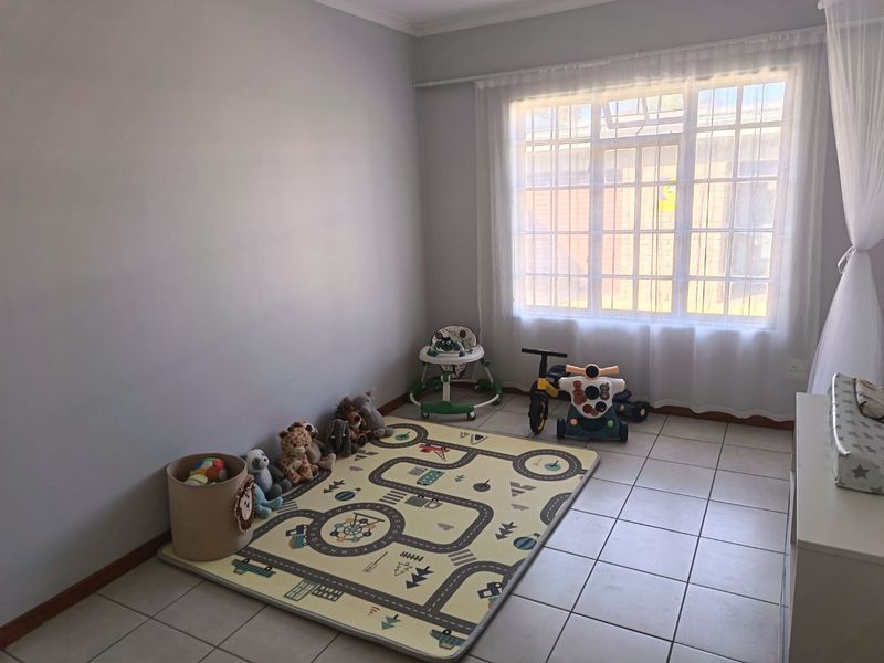 A bright bedroom featuring neutral wall tones, tiled flooring, and a large window with security bars, providing ample natural light.