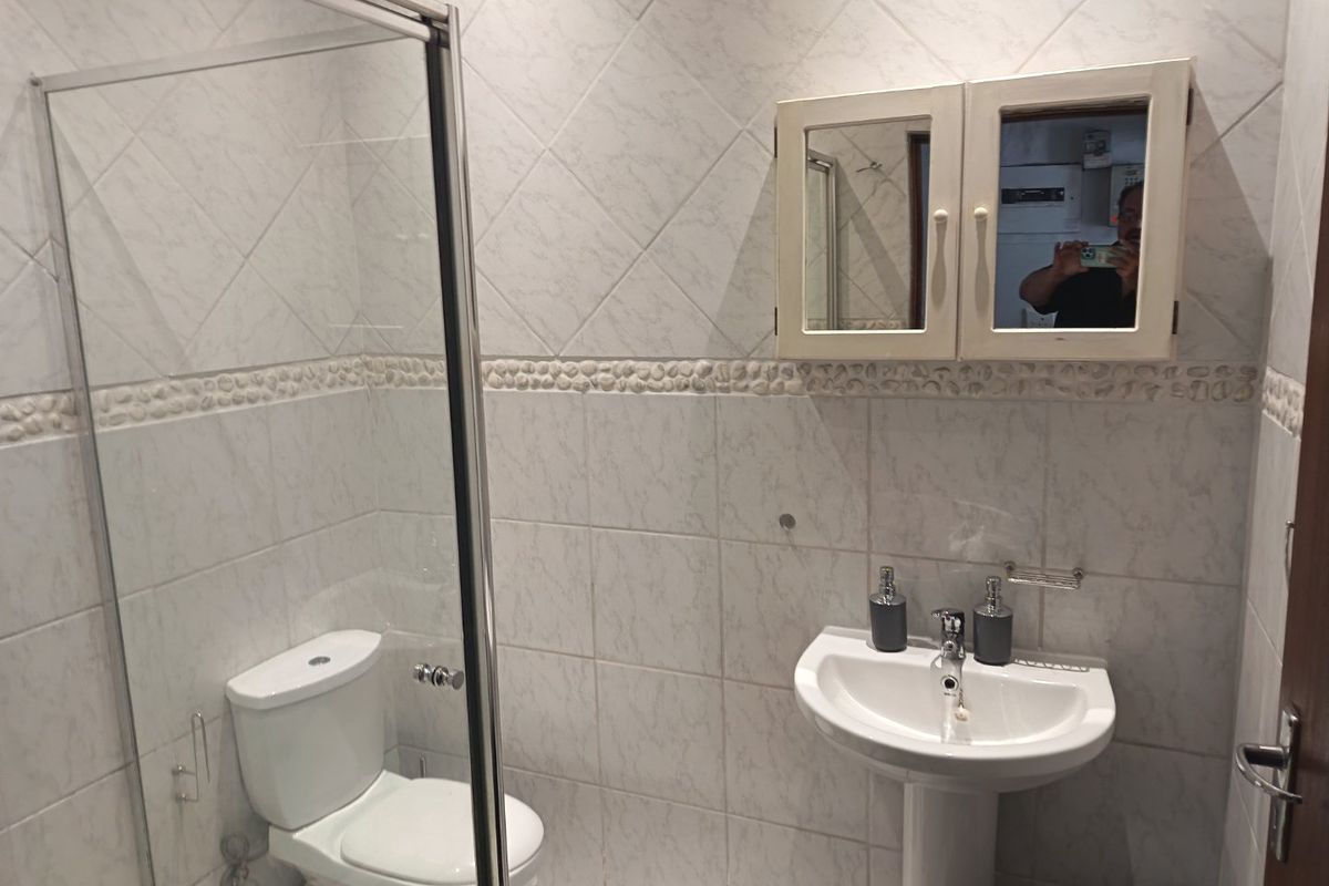 A functional bathroom featuring a pedestal basin, a glass-enclosed shower, and a wall-mounted medicine cabinet with tiled wall finishes.