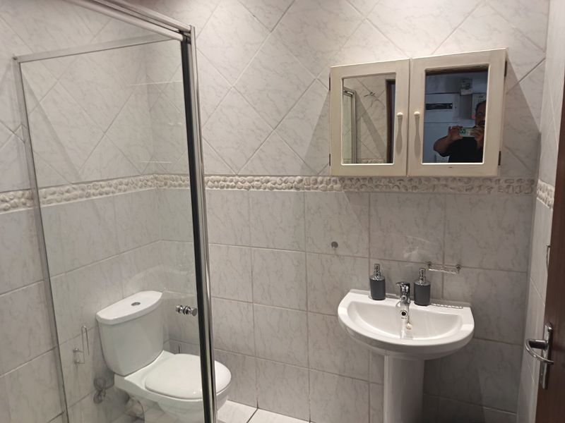 A functional bathroom featuring a pedestal basin, a glass-enclosed shower, and a wall-mounted medicine cabinet with tiled wall finishes.