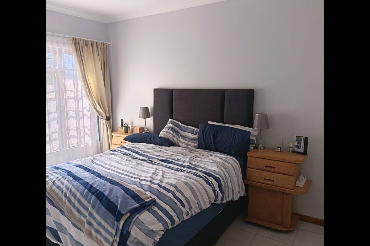 A functional bedroom featuring tiled flooring and natural light through a window with curtain rails.