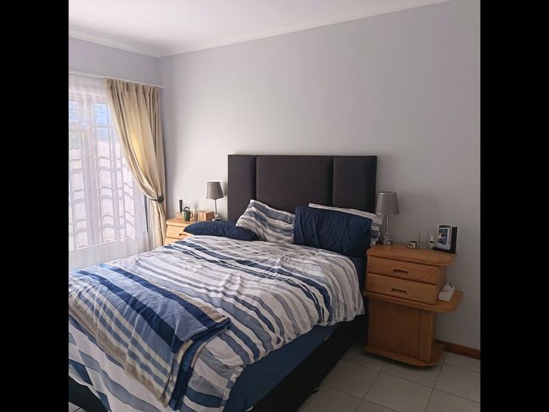 A functional bedroom featuring tiled flooring and natural light through a window with curtain rails.