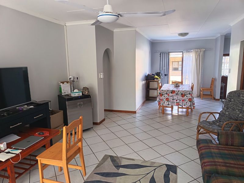 Open-plan living and dining area featuring ceramic floor tiles, a ceiling fan, and access to the exterior through a security gate.