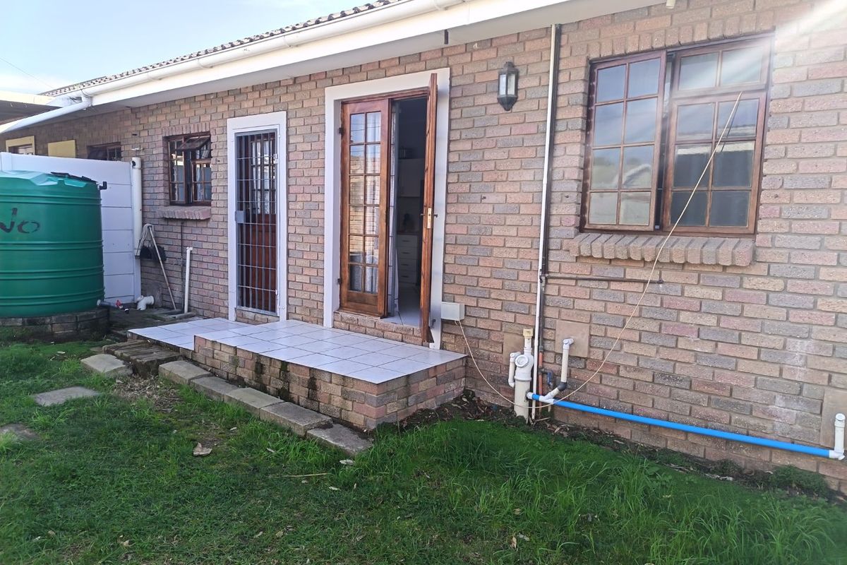 Rear exterior view of a face brick house featuring a small tiled patio, security gate, timber framed doors, and a large water storage tank.
