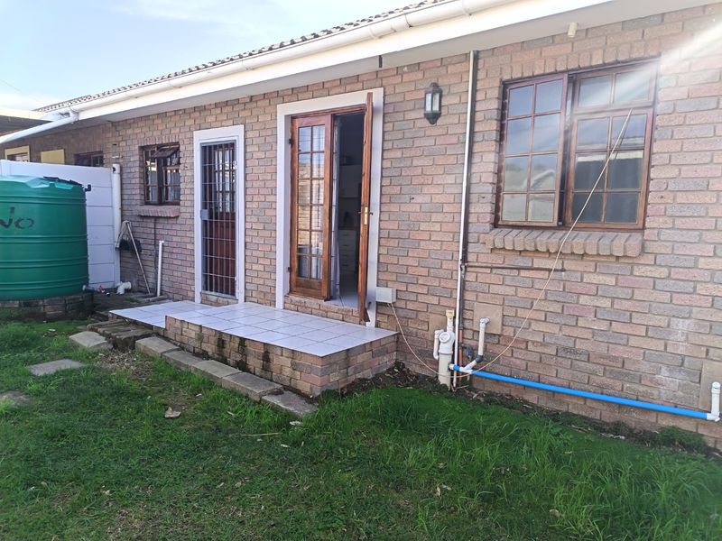 Rear exterior view of a face brick house featuring a small tiled patio, security gate, timber framed doors, and a large water storage tank.