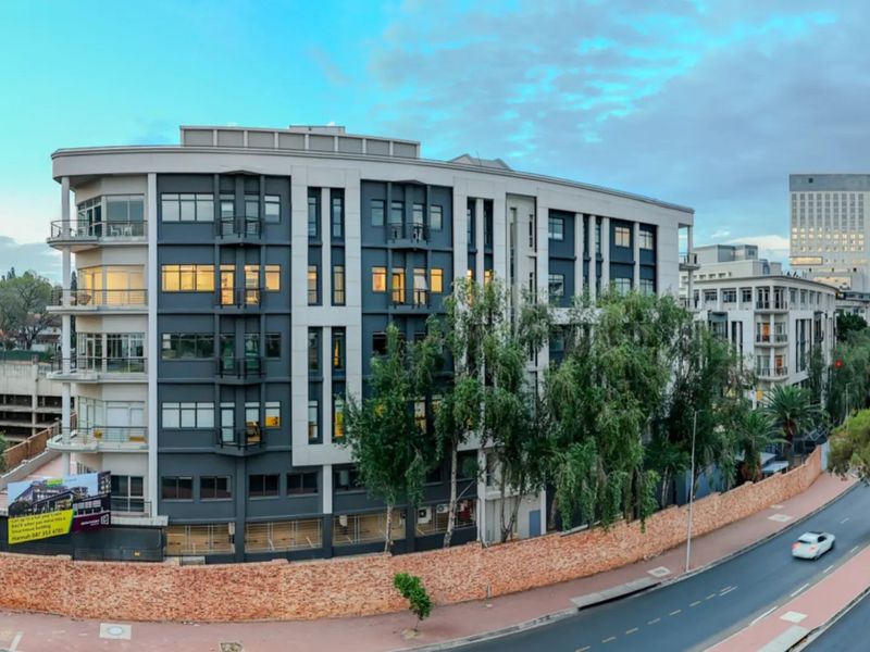 A panoramic view of a modern multi-story commercial building featuring a contemporary facade, balconies, and a secure perimeter brick wall along the street.