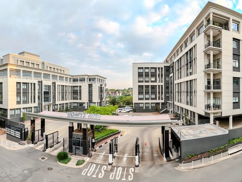 Wide-angle view of the Sandown Mews commercial office park entrance, featuring modern multi-story buildings, secure boom gate access, and well-maintained paved driveways.