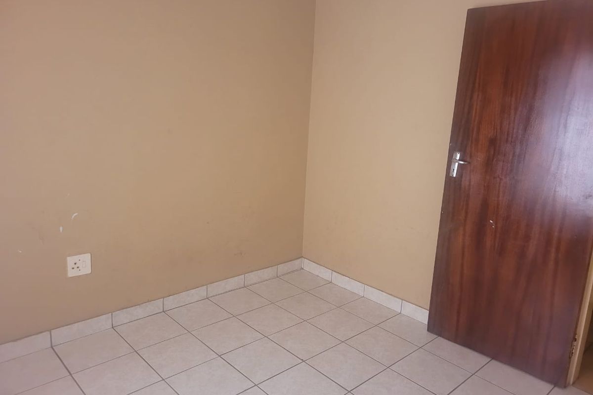 An empty bedroom featuring neutral wall paint, tiled flooring, and a wooden door.