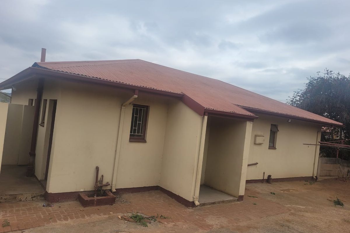 Rear view of a single-story house featuring a corrugated metal roof, brick paved area, and exterior wall finishes requiring maintenance.