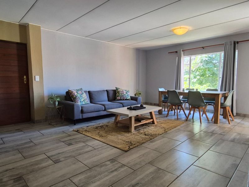 Spacious open-plan living and dining area featuring modern tiled flooring, neutral wall tones, and natural light from a large window.