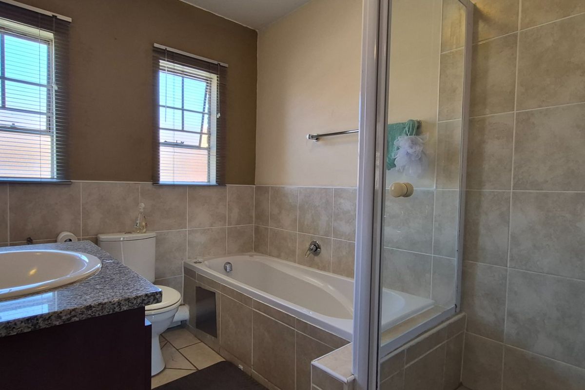 A functional bathroom featuring a built-in vanity with granite countertop, a separate bathtub, and a glass-enclosed shower with neutral wall tiling.