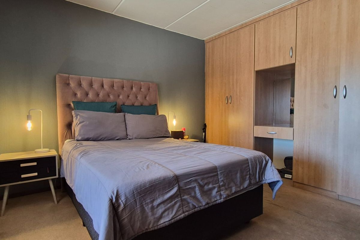 A comfortable bedroom featuring a large built-in wardrobe with integrated vanity space and neutral carpeted flooring.