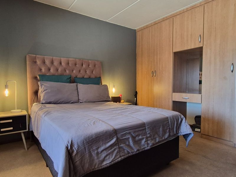 A comfortable bedroom featuring a large built-in wardrobe with integrated vanity space and neutral carpeted flooring.