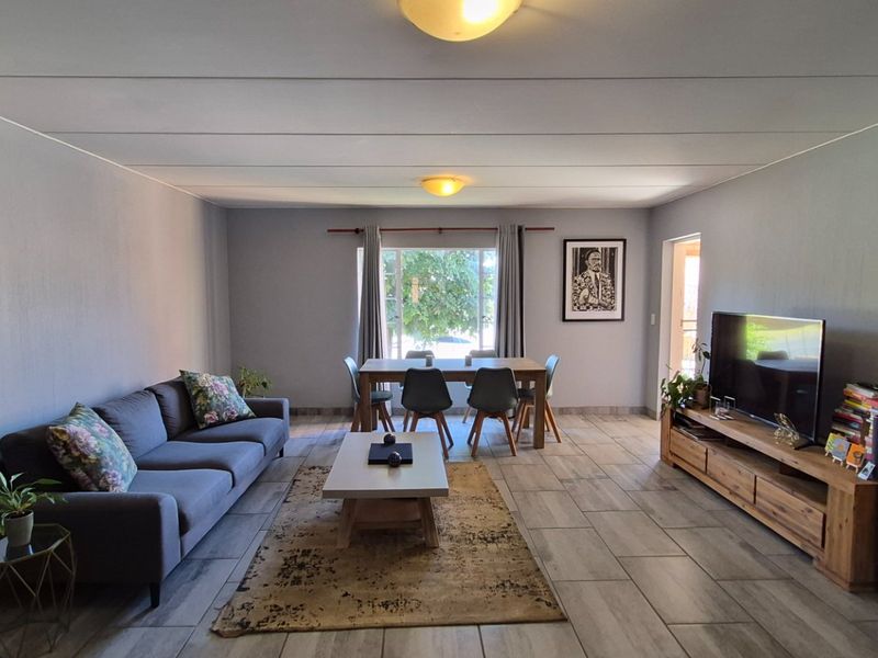 Spacious open-plan living and dining area featuring neutral wall tones, tiled flooring, and natural light through a rear window.