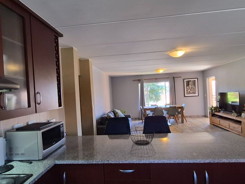 Open-plan living area featuring a kitchen with granite countertops and dark wood cabinetry, flowing into a dining and lounge space with tiled flooring.