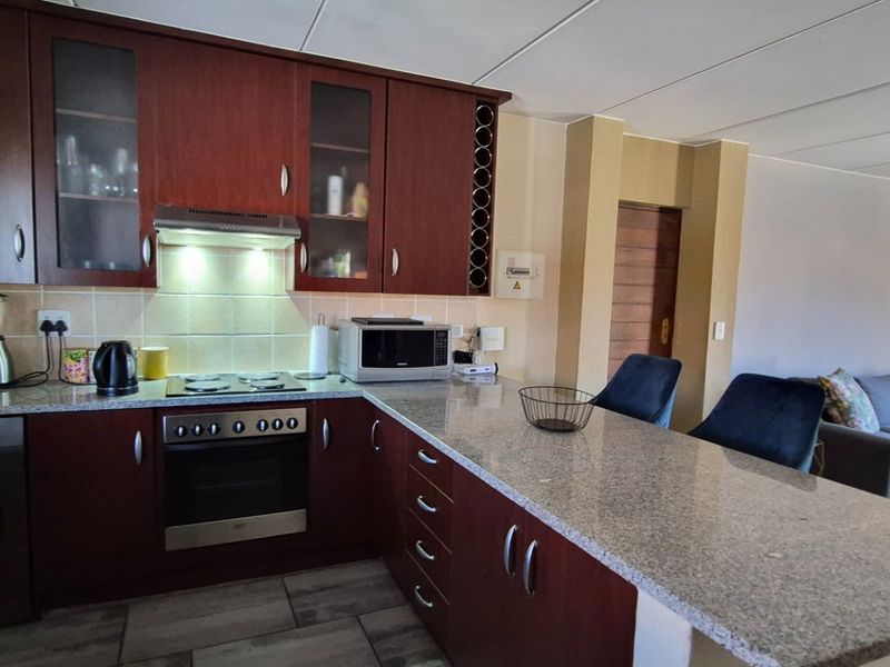 Open-plan kitchen and living area featuring dark wood cabinetry, granite countertops, built-in appliances, and a breakfast bar, flowing into the adjacent lounge space.