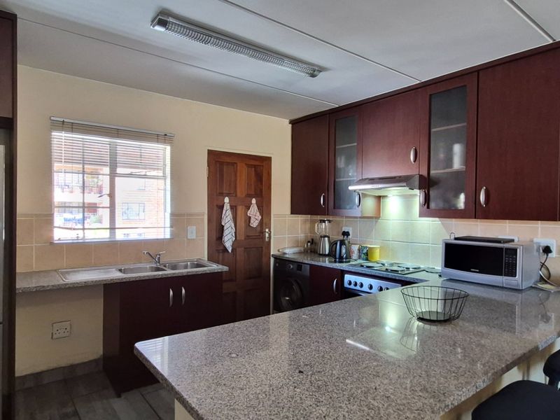 Functional kitchen featuring dark wood cabinetry, granite countertops, a breakfast nook, and a tiled backsplash with integrated appliances.