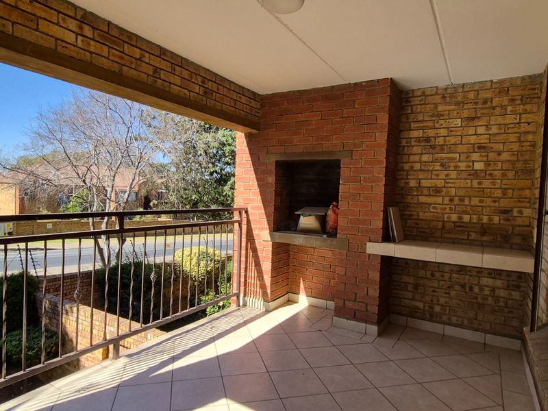 A covered balcony featuring a built-in brick braai, tiled flooring, and a metal balustrade, offering an outdoor space for relaxation and entertaining.