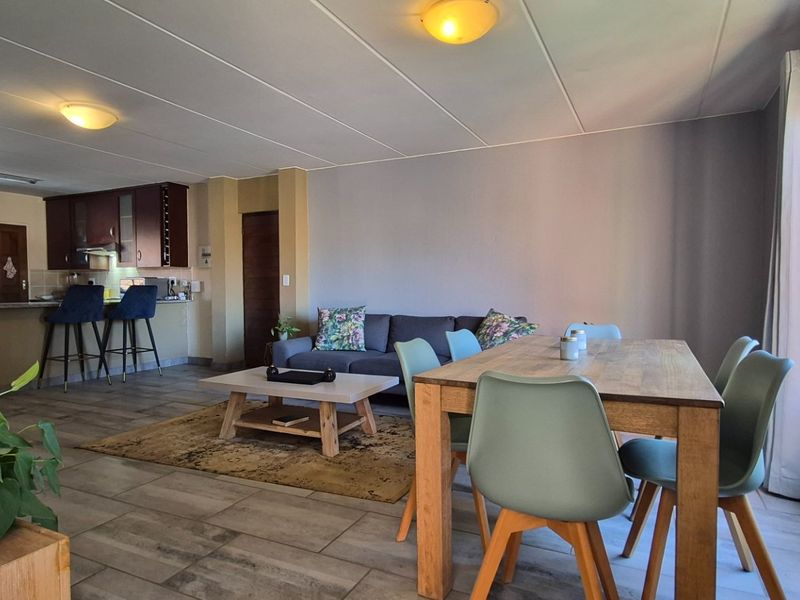 Spacious open-plan living and dining area featuring tiled flooring, integrated kitchen cabinetry with an island, and ample natural light from large windows.