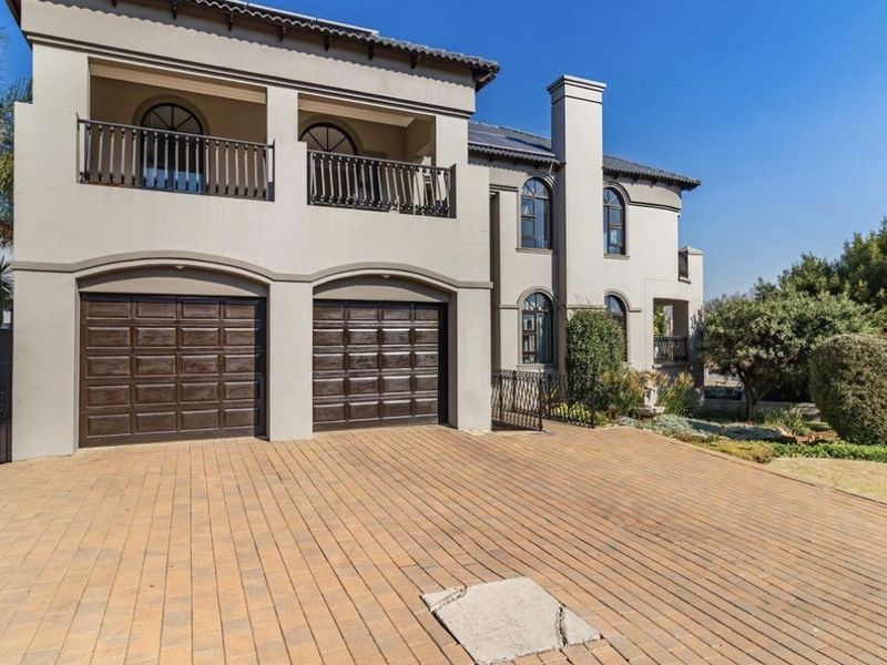 Front elevation of a multi-story residence featuring a double garage, paved driveway, and an upper-level balcony with wrought iron railings.