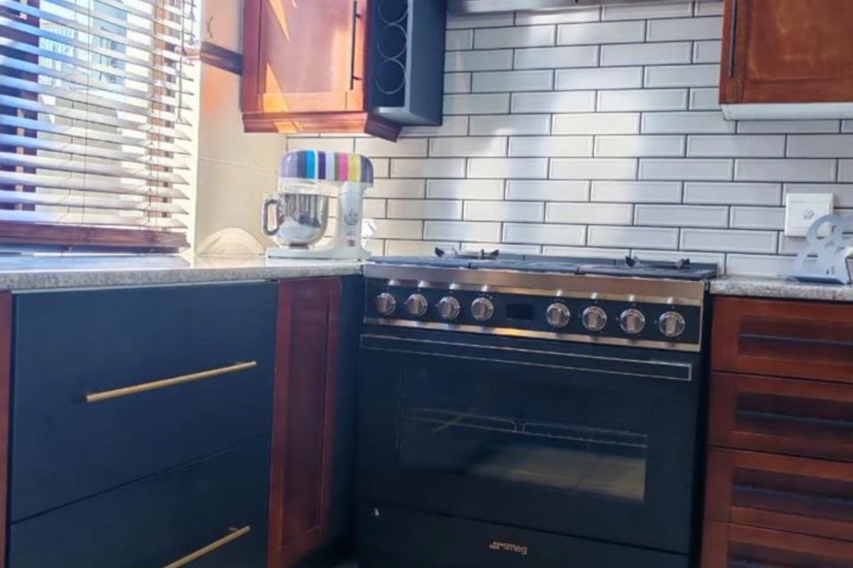 A well-maintained kitchen featuring a black Smeg gas stove, stainless steel extractor fan, subway tile backsplash, and contrasting dark wood and matte cabinetry.