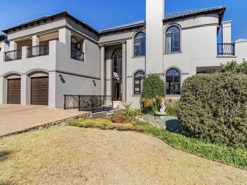 A grand double-story residence featuring a paved driveway, double garage, arched windows, and upper-level balconies with wrought iron railings.