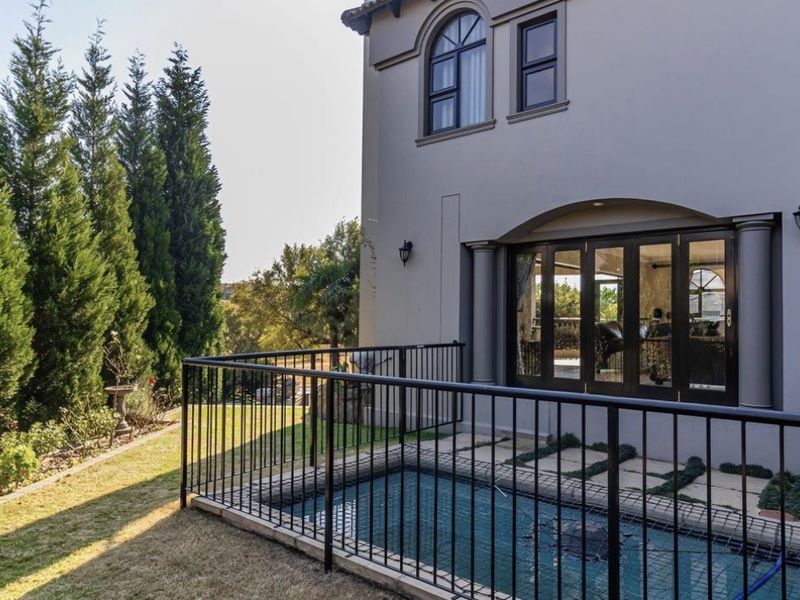 A well-maintained rear exterior area featuring a swimming pool with safety fencing, paved patio space, and access to the home via bi-fold doors.