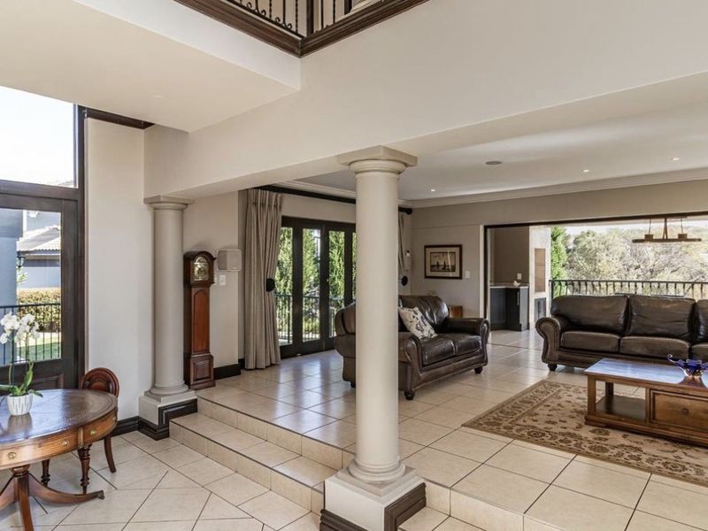 Spacious open-plan living area featuring tiled floors, structural columns, and a double-height ceiling with access to an outdoor balcony.