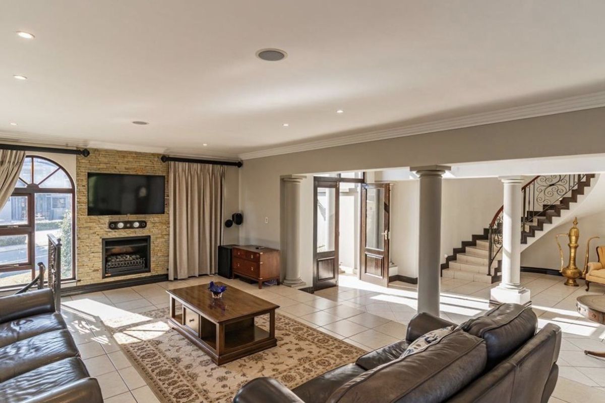 Spacious living area featuring a stone-clad fireplace, tiled flooring, recessed lighting, and an elegant staircase with wrought iron detailing.
