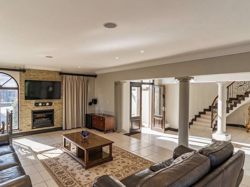 Spacious living area featuring a stone-clad fireplace, tiled flooring, recessed lighting, and an elegant staircase with wrought iron detailing.