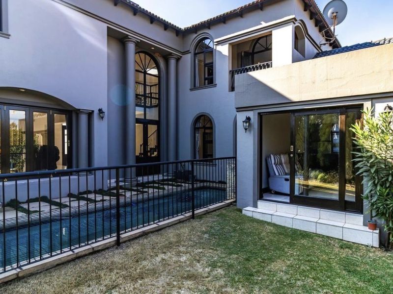 Rear exterior view of a multi-story home featuring a swimming pool with safety fencing, arched architectural windows, and a paved patio area.