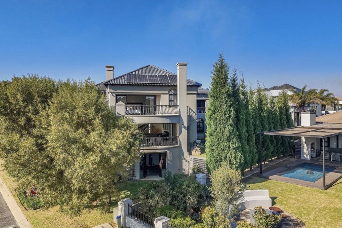 Rear view of a multi-story house featuring multiple balconies, solar panels, a swimming pool, and a covered patio area within a landscaped garden.