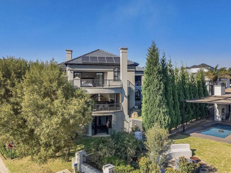 Rear view of a multi-story house featuring multiple balconies, solar panels, a swimming pool, and a covered patio area within a landscaped garden.