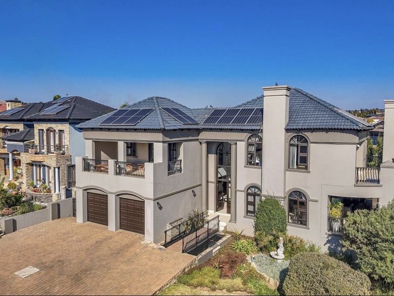Aerial view of a large two-story residential property featuring a paved driveway, double garage, solar panels, and multiple balconies.