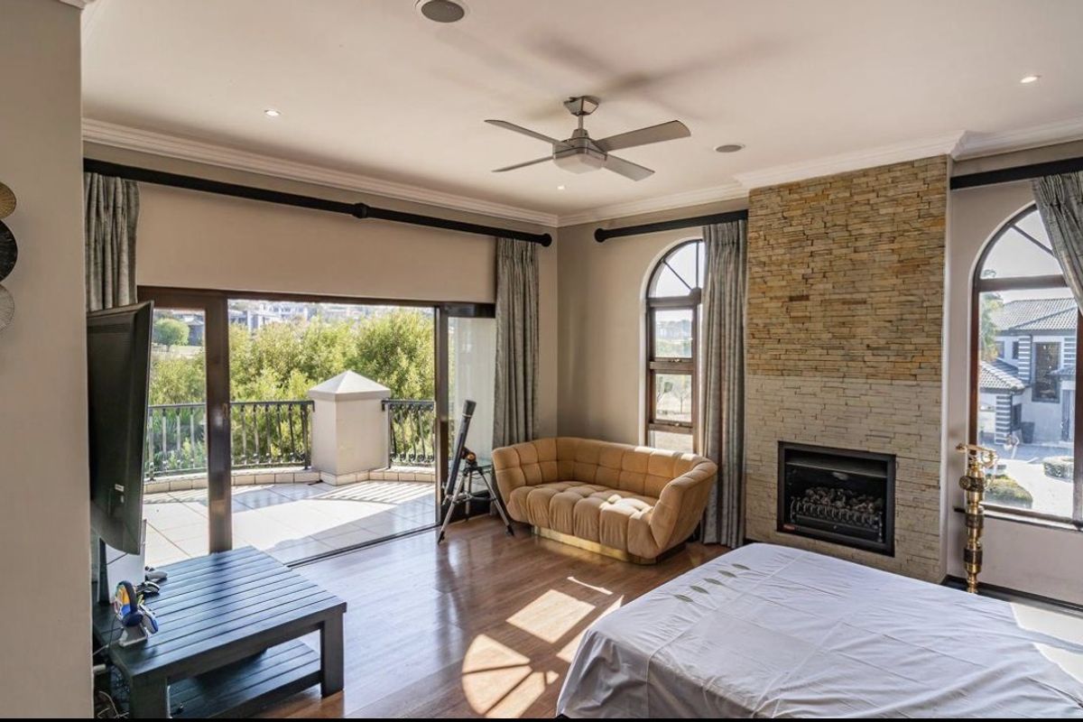 Spacious bedroom featuring a stone-clad fireplace, hardwood flooring, ceiling fan, and large sliding doors opening onto a private balcony.