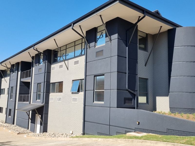 Modern commercial building exterior featuring a contemporary dark grey and light brick facade with clean architectural lines and paved driveway access.
