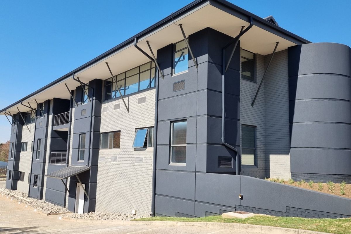 Modern commercial building exterior featuring a contemporary dark grey and light brick facade with clean architectural lines and paved driveway access.
