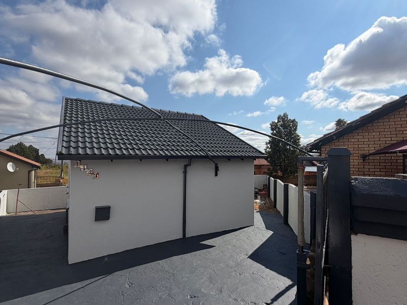 A view of the front exterior of the house featuring a tiled roof, freshly painted walls, and a paved driveway area.