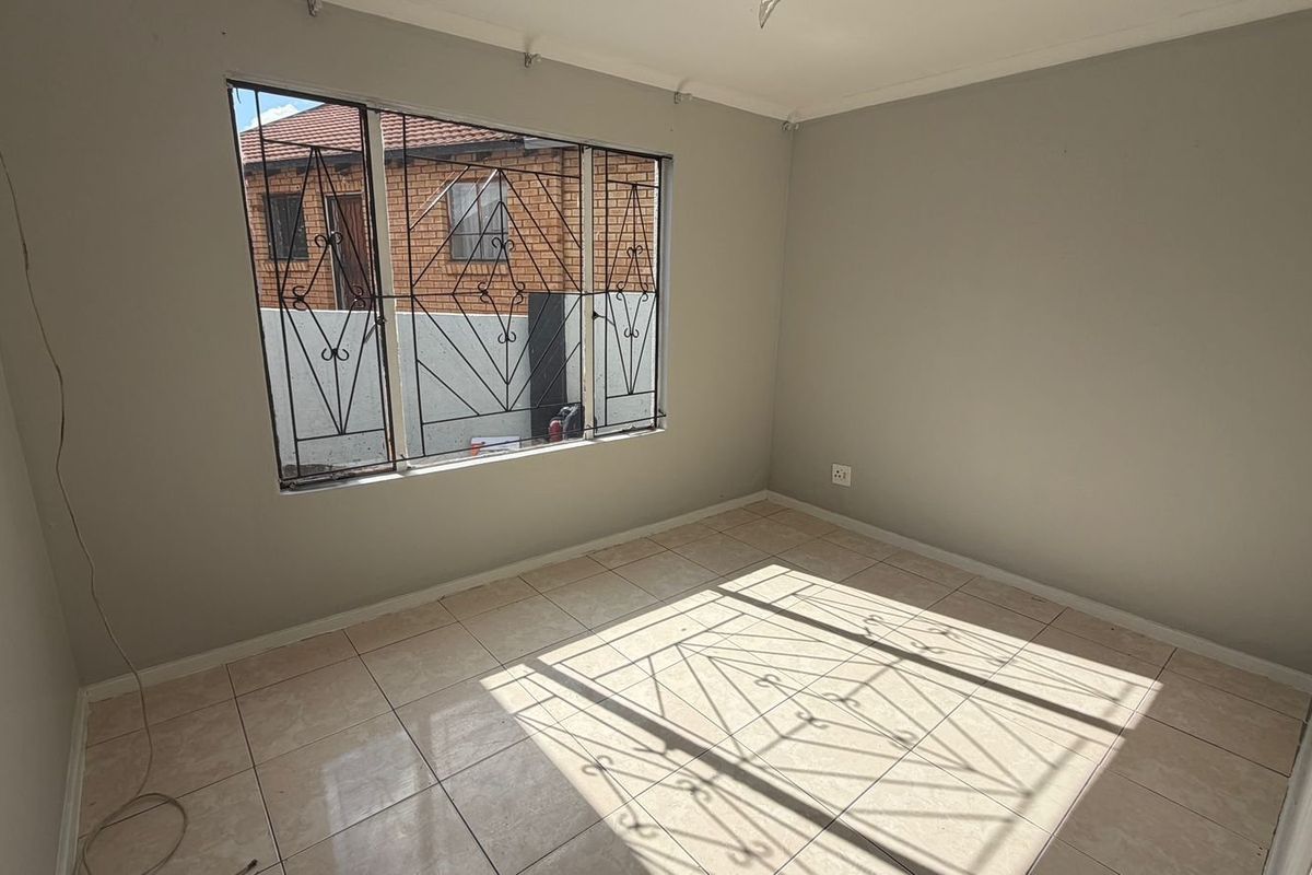A vacant bedroom featuring neutral tiled flooring, grey walls, and security bars on the window.