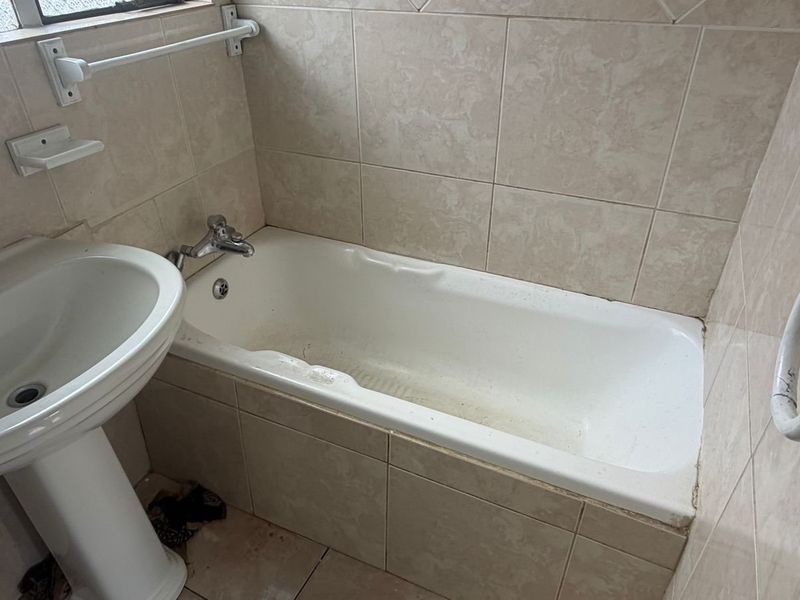 A dated bathroom featuring a pedestal basin and a built-in bathtub with tiled surrounds, requiring cosmetic updates to improve its condition.