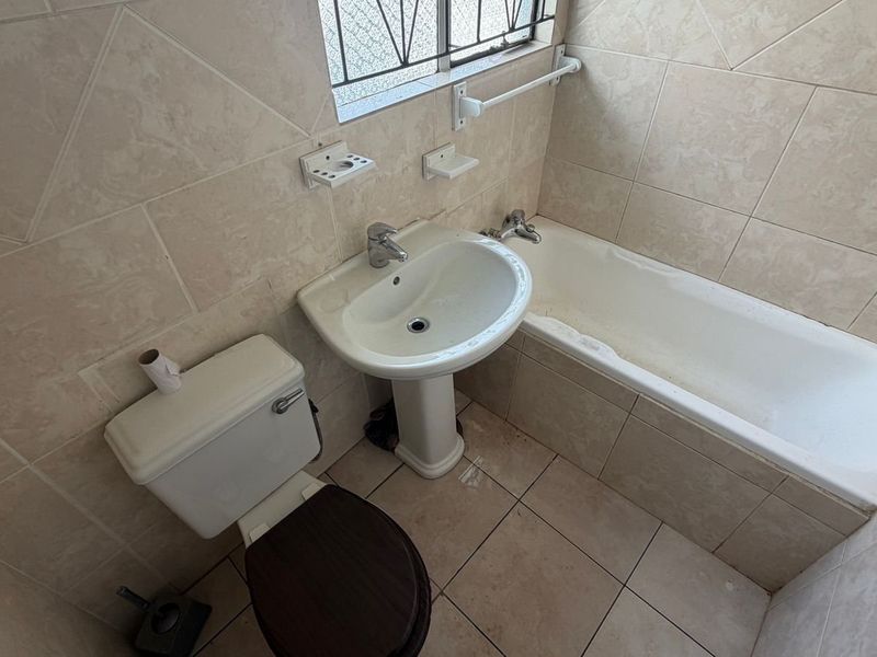 A compact bathroom featuring a pedestal basin, bathtub, and toilet with neutral ceramic wall and floor tiling.
