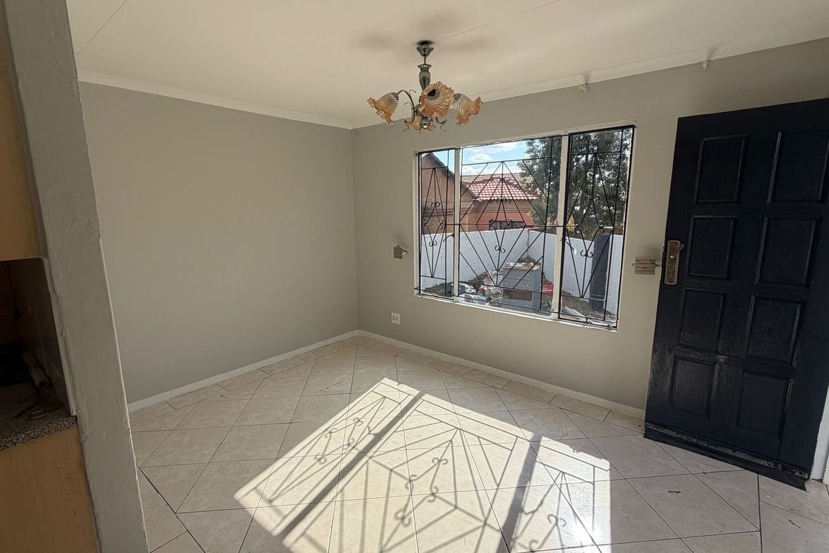 An empty living area featuring tiled flooring, a security-gated window, and a panel door, offering a blank canvas for interior design.