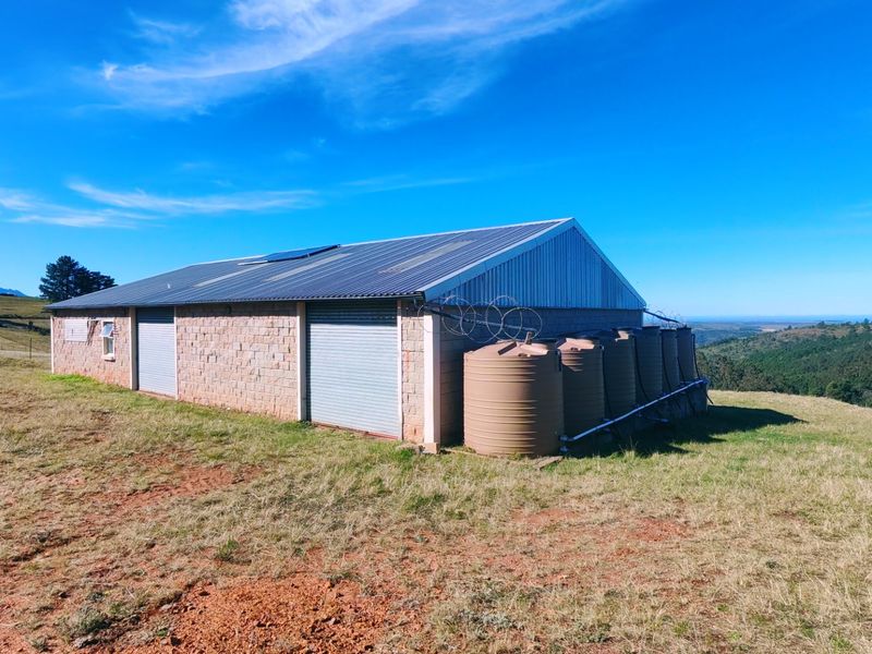 A functional farm outbuilding featuring concrete block construction, roller shutter doors, and a series of external water storage tanks on a rural landscape.
