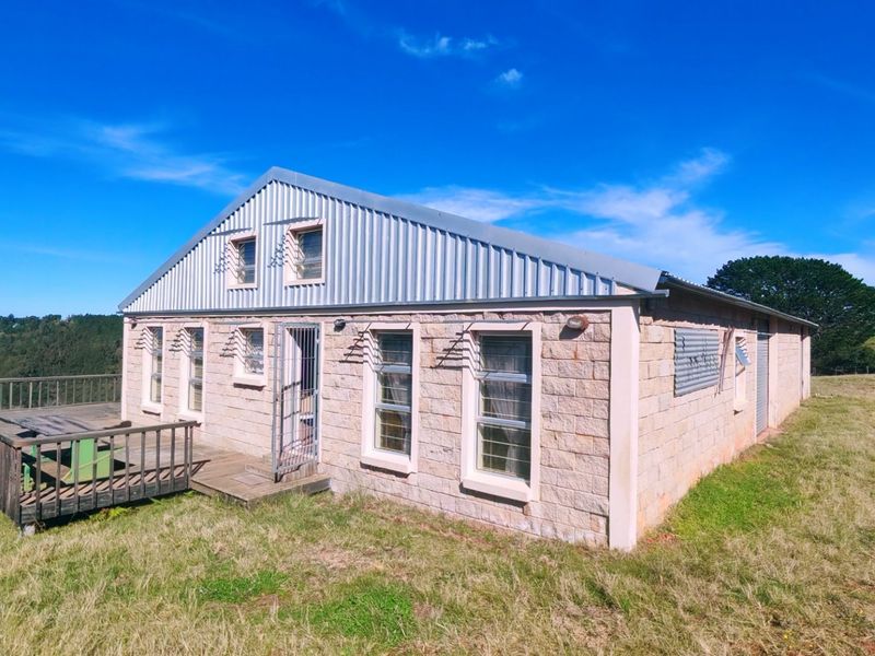 Rear view of a stone-clad farm building featuring a corrugated metal roof and an attached timber deck overlooking the surrounding landscape.