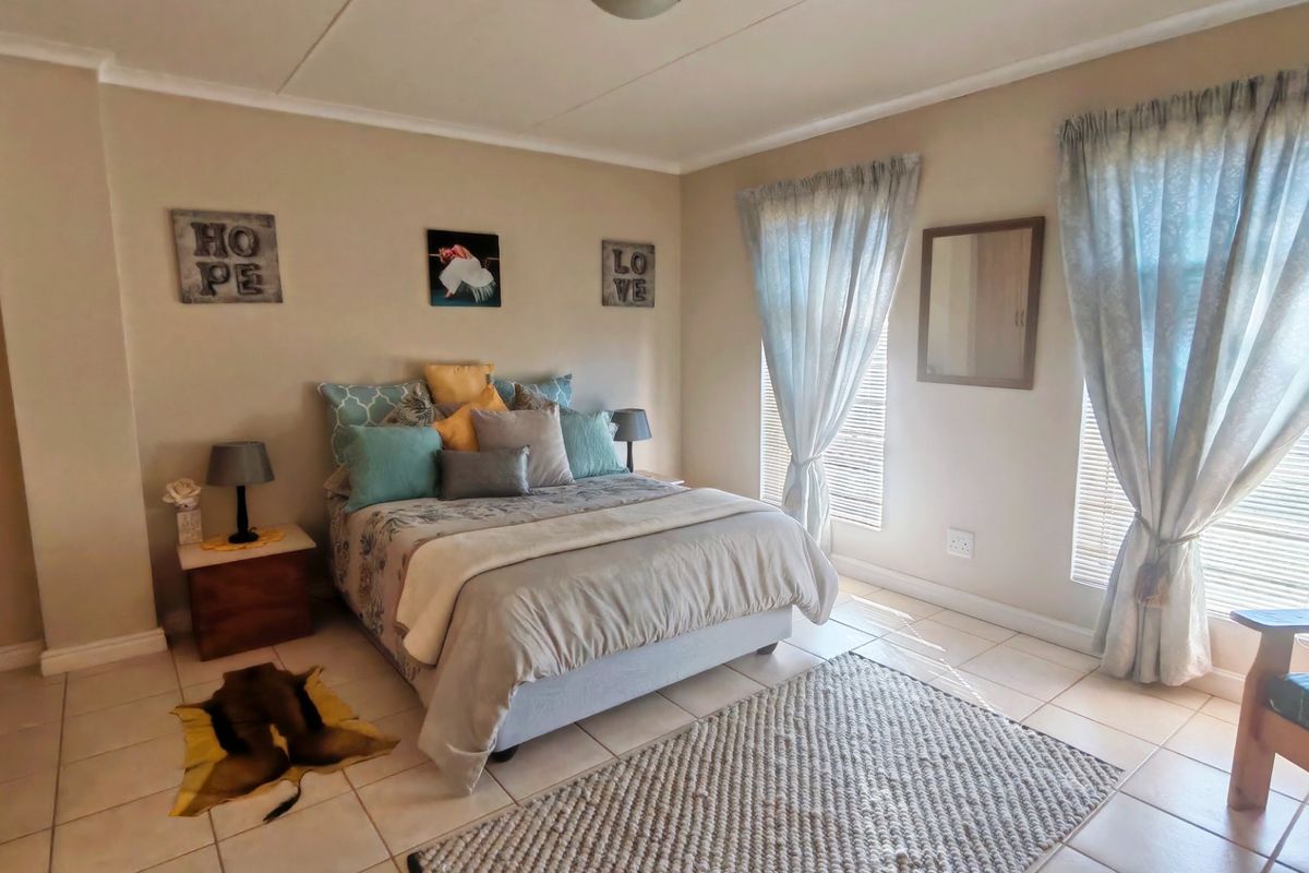 A well-maintained bedroom featuring neutral wall tones, tiled flooring, and dual windows with curtains and blinds, providing a bright and comfortable living space.