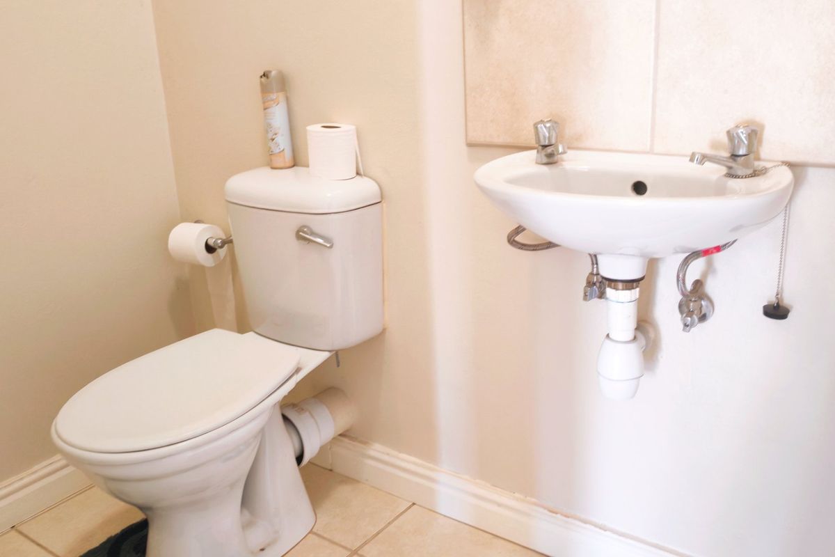 A functional bathroom featuring a standard toilet and a wall-mounted basin with exposed plumbing fixtures.