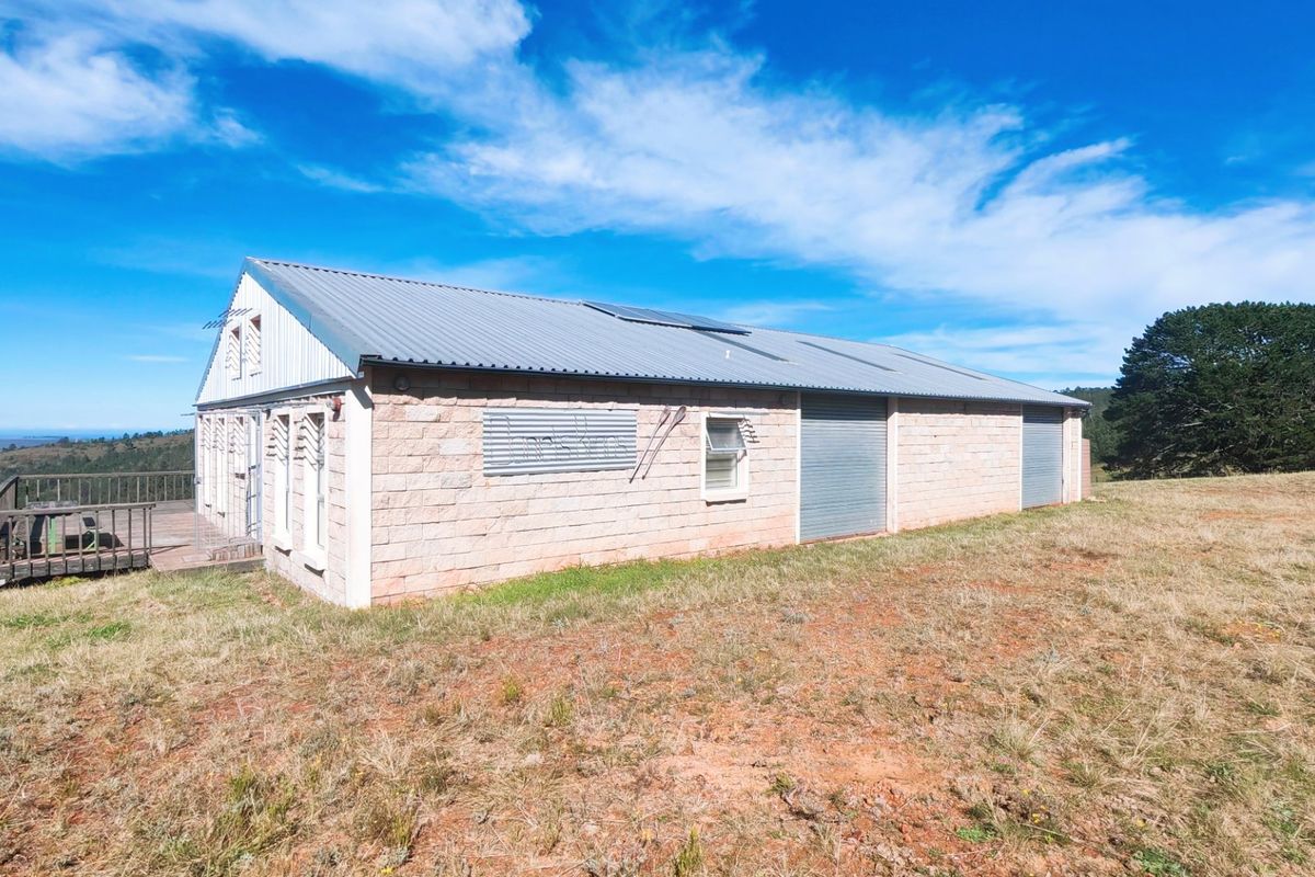 Rear view of a stone-clad farm building featuring a corrugated metal roof, solar panels, roller shutter doors, and an attached timber deck.