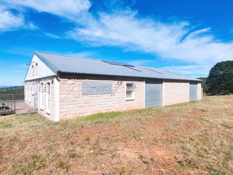 Rear view of a stone-clad farm building featuring a corrugated metal roof, solar panels, roller shutter doors, and an attached timber deck.