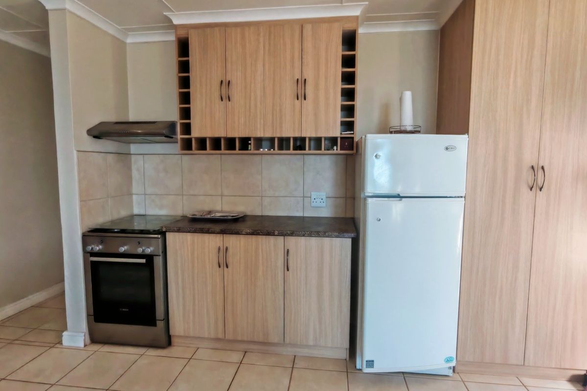 A functional kitchen featuring light wood-finish cabinetry, tiled backsplash, laminate countertops, and ceramic floor tiles, providing a practical and well-maintained cooking space.