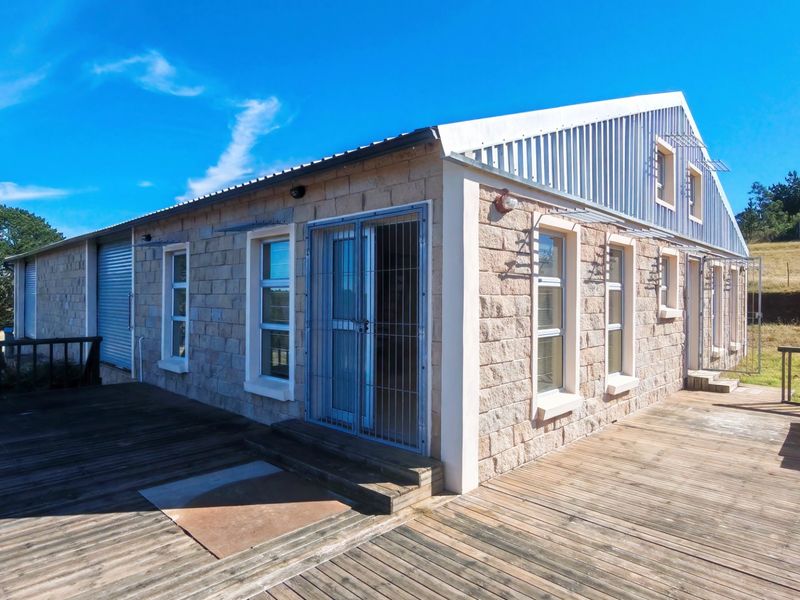 Rear view of a stone-clad farm building featuring a corrugated metal roof and extensive timber decking, set against a rural landscape.