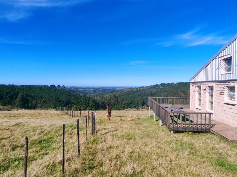 Rear view of a farm property featuring a timber deck, stone-clad exterior, and expansive rural landscape views.